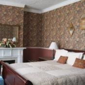 Guest room, cherry bed frame, brown floral wall paper, white fire place